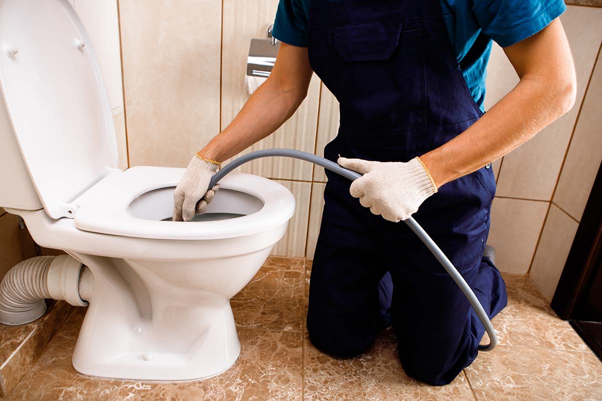 A plumber using a plumbing snake to demonstrate how to unclog a toilet properly.