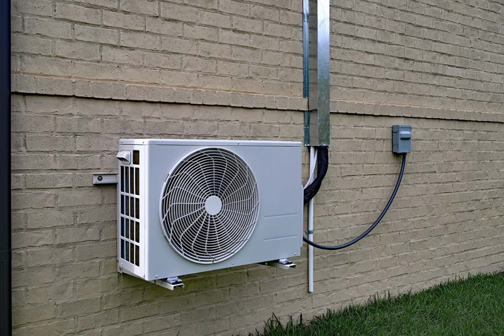 An outdoor air conditioning unit affixed to a brick wall, demonstrating Lund Plumbing and Heating's reliable cooling services for summer comfort in Melrose, Massachusetts.