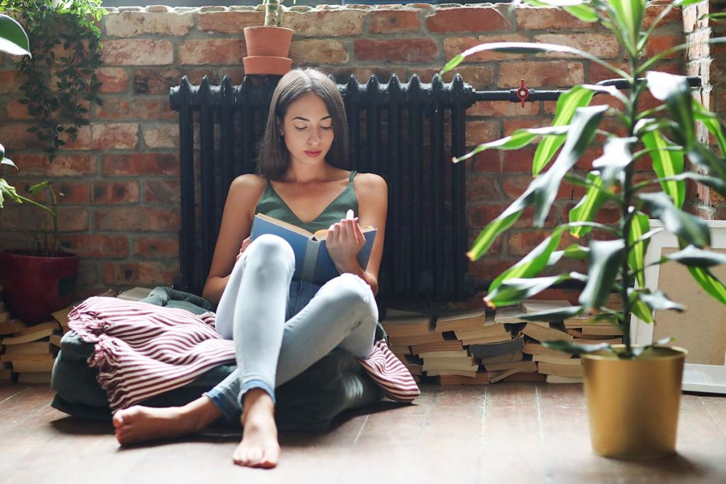 A young woman peacefully reading by a classic radiator, benefiting from the reliable and efficient heating solutions provided by Lund Plumbing and Heating in Cambridge, Massachusetts