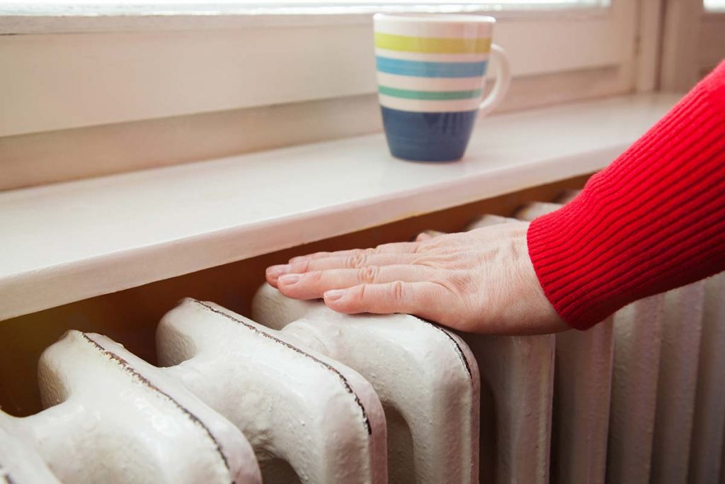 A person enjoying the warmth coming from their radiator, exemplifying the comfort that Lund Plumbing and Heating provides for their customers in Winchester, Massachusetts