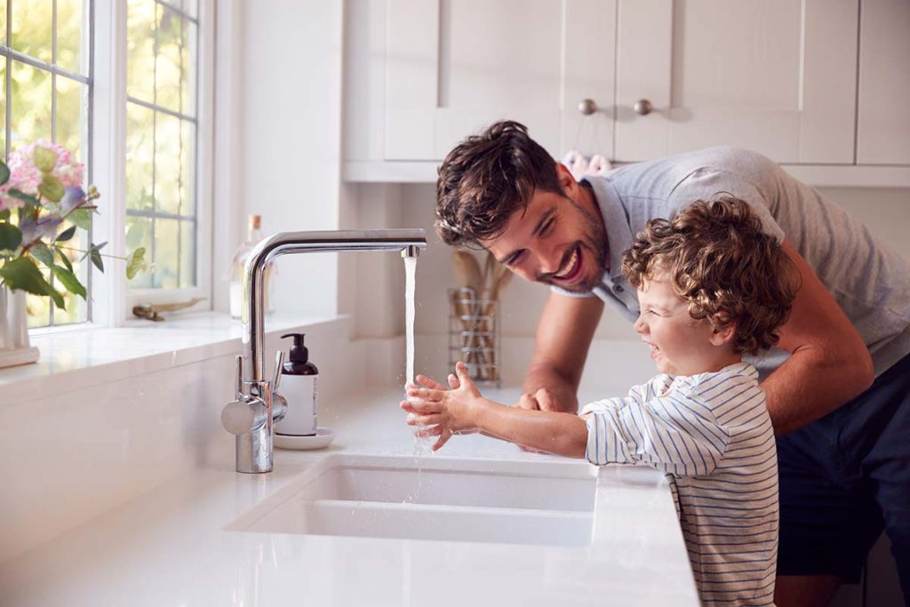 A father and son at the kitchen sink showcasing the modern plumbing installations by Lund Plumbing and Heating in Belmont, Massachusetts.