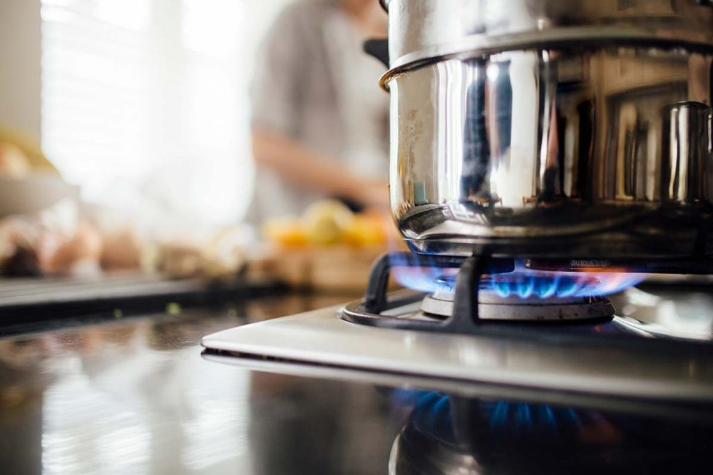 A pot on a stove with a blue flame, illustrating the safe and dependable gas plumbing services Lund Plumbing and Heating delivers in Lexington, Massachusetts.