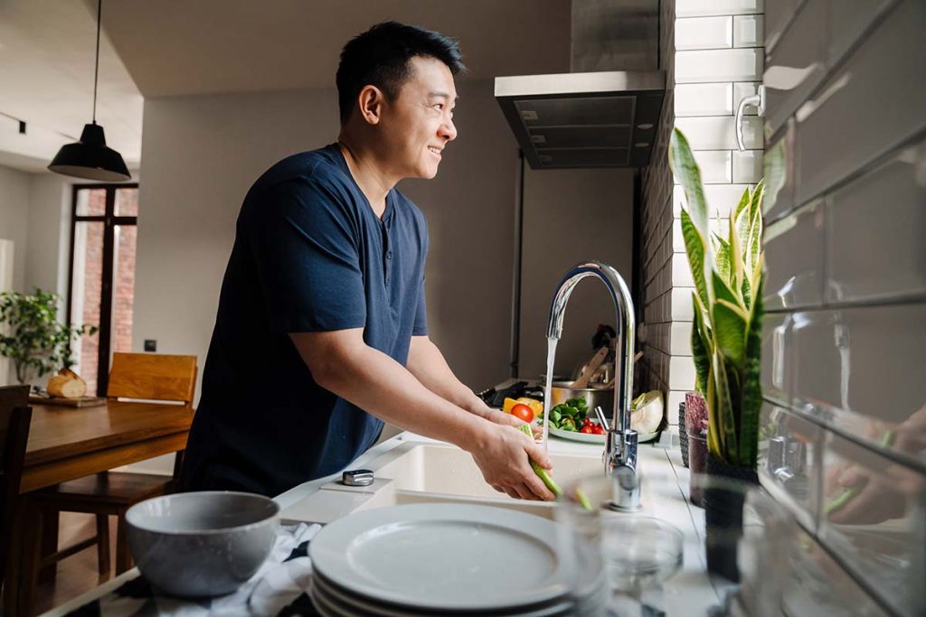 A man washing vegetables at the kitchen sink, highlighting the importance of quality plumbing services provided by Lund Plumbing and Heating in Malden, Massachusetts.