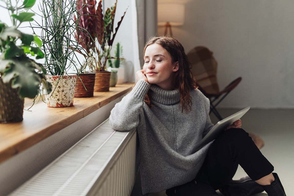 A serene woman sitting by the window with a tablet, possibly reading positive customer reviews about Lund Plumbing and Heating's services in Lexington, Massachusetts.