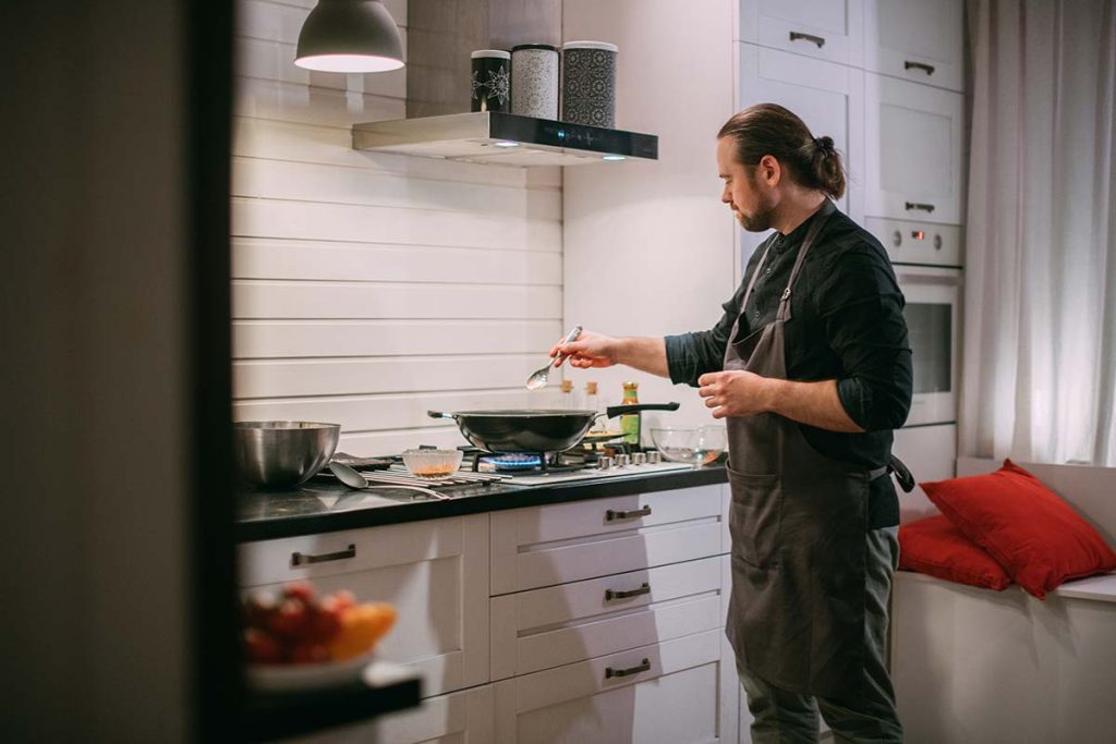 A man focused on cooking in a well-equipped kitchen, symbolizing the satisfaction of customers with Lund Plumbing and Heating's services in Melrose, Massachusetts.