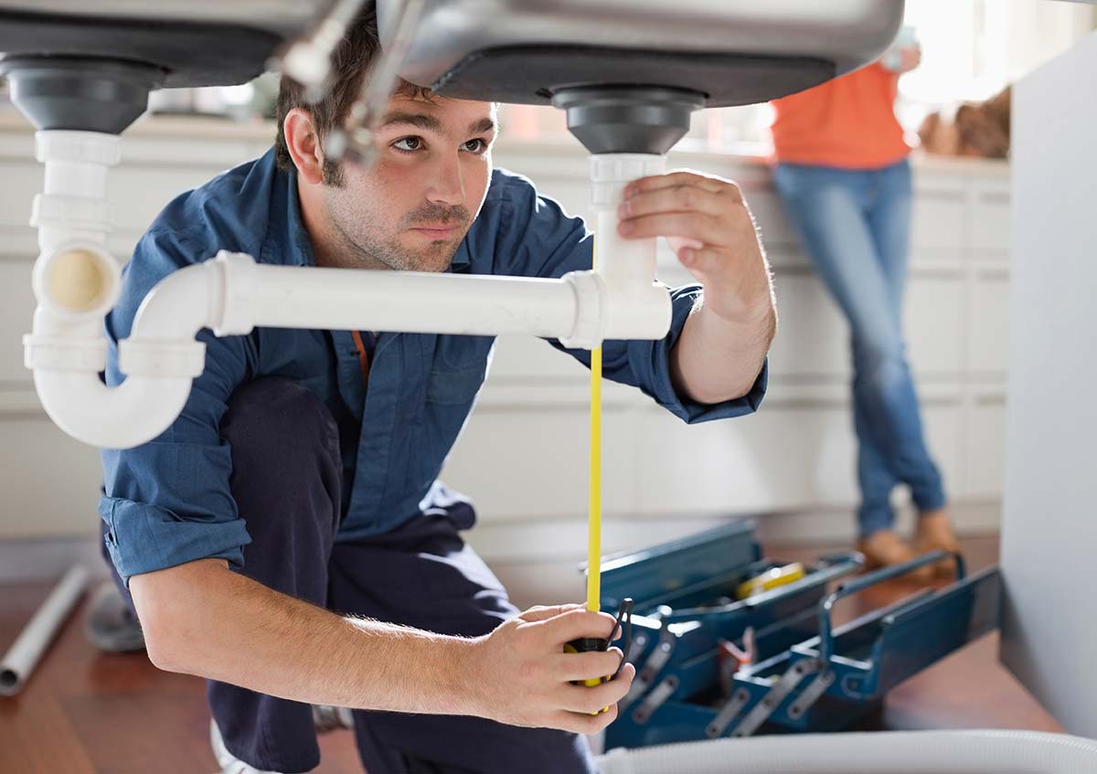 A kitchen plumber inspecting pipes under a kitchen sink, with tools nearby.