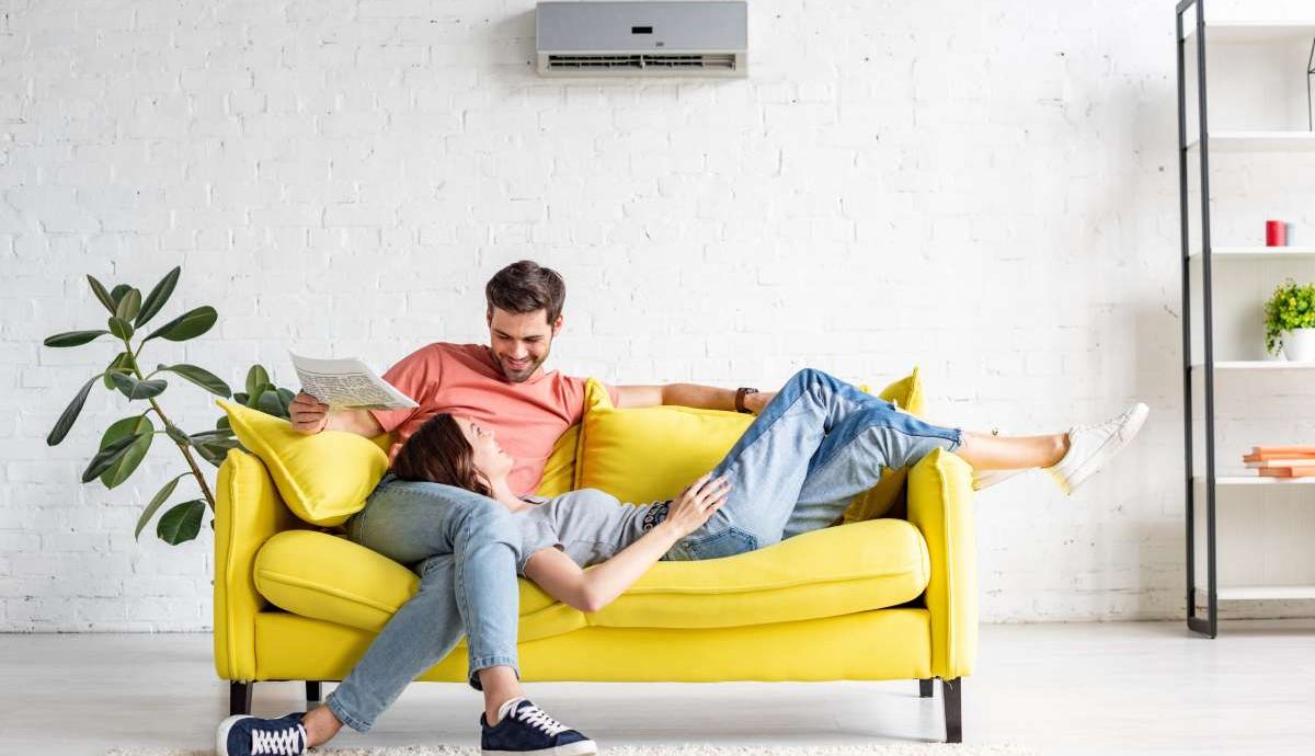 This images illustrates life after Lund's Tewksbury Air Conditioning Servoce - A happy man with smiling girlfriend relaxing on yellow sofa under air conditioner at home